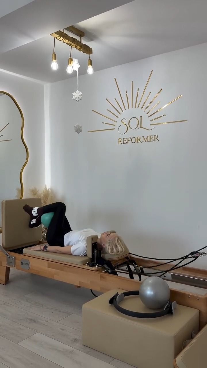 Clientă pe reformer cu picioarele în chingi, în studioul SOL Reformer